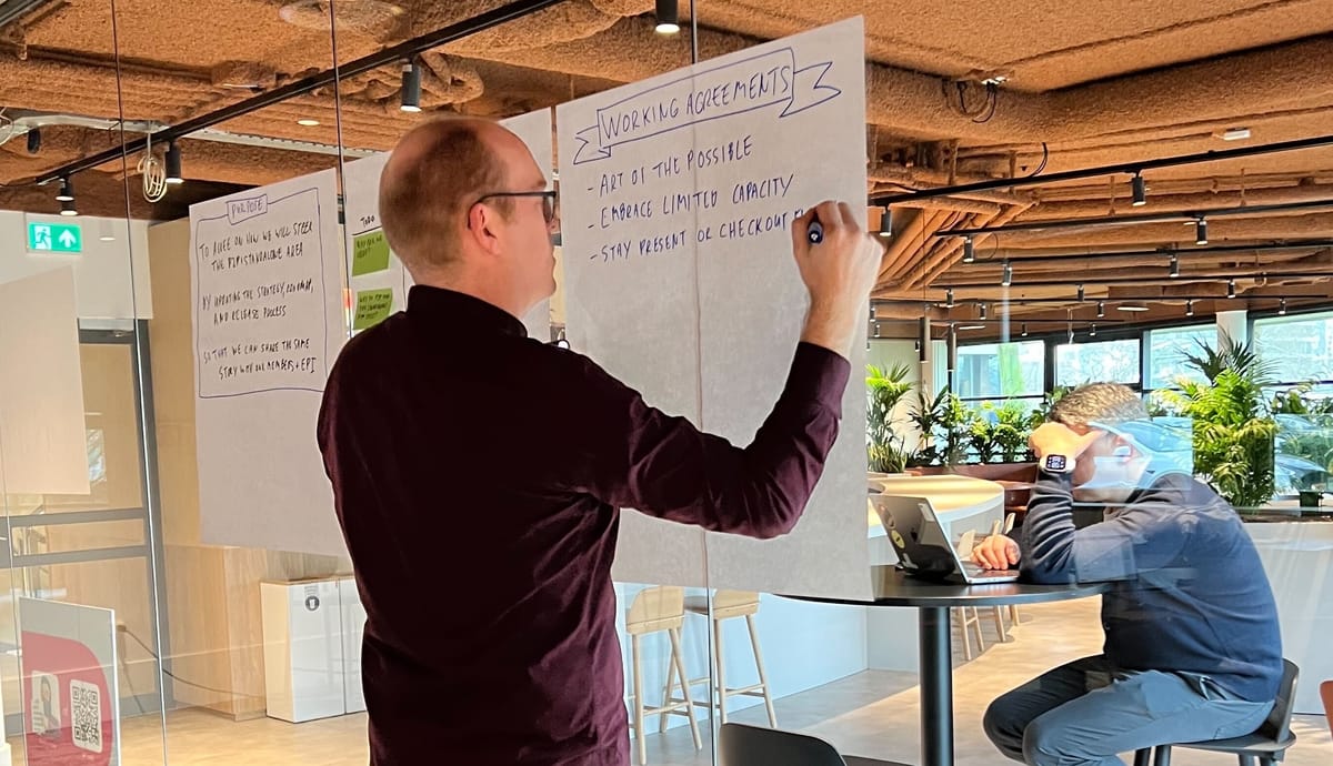 Alex writing on a flipchart page stuck to a glass wall